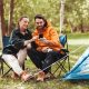 camping, tourism and travel concept - happy couple with smartphone drinking tea at campsite